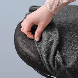 Hand adjusts a textured fabric cover on a circular stool seat, demonstrating easy-to-use and practical upholstery for home decor