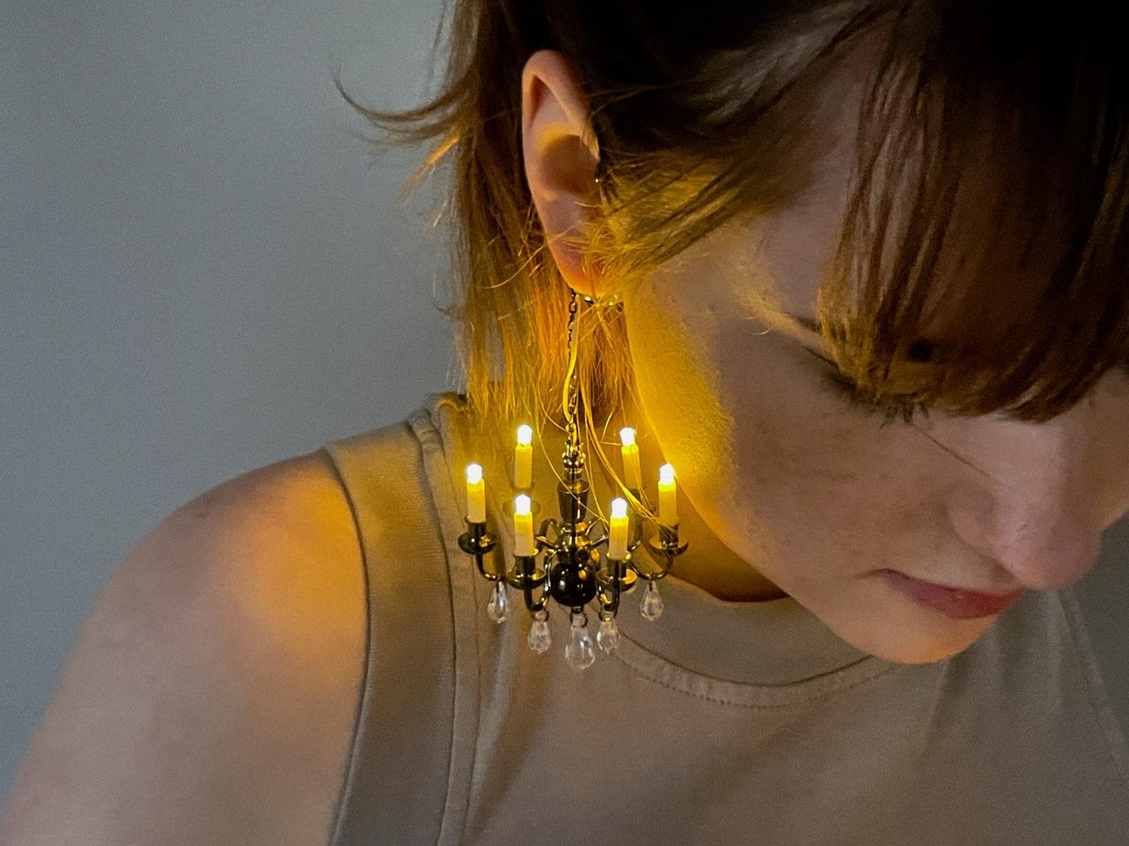 Person wearing unique chandelier earrings with glowing candle-like lights