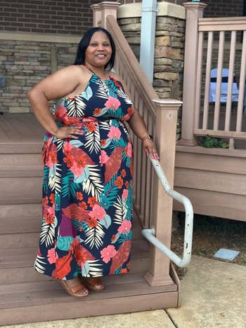 reviewer poses on stairs in floral-patterned halter maxi dreess