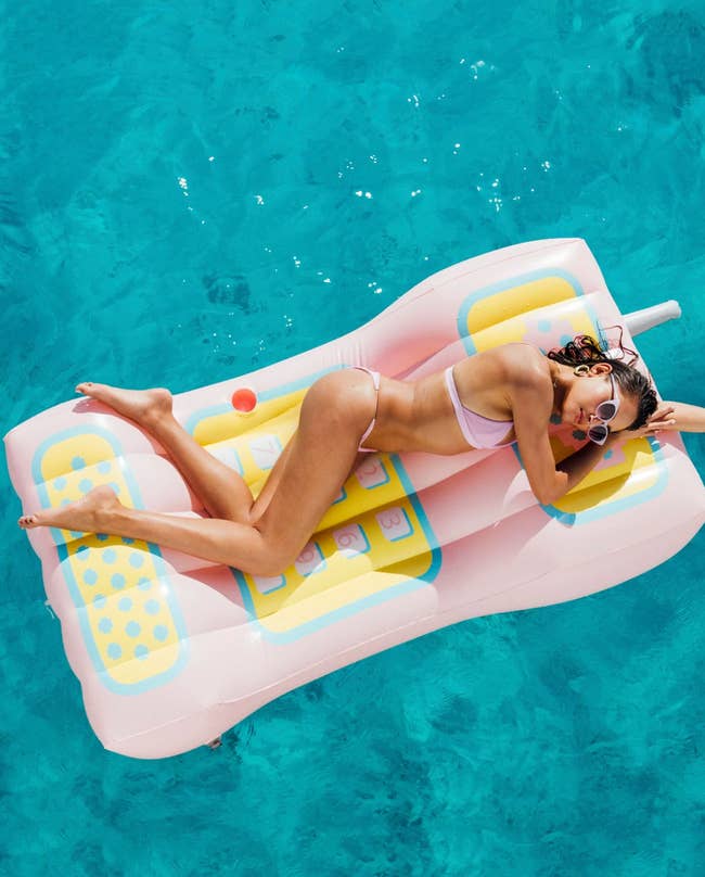 model lounging on pink retro phone-shaped float in pool 