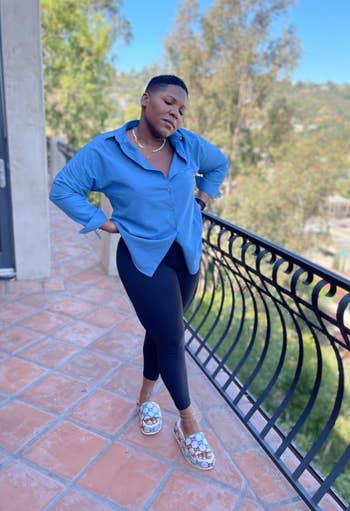 Person poses connected  a balcony wearing a escaped   bluish  shirt, achromatic  leggings, and patterned sandals, with trees successful  the background