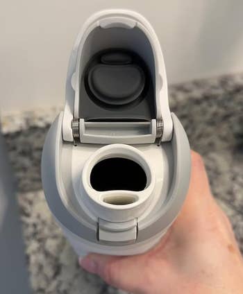 Person holding a white and gray insulated water bottle with a flip-top lid open, showing the spout, on a granite countertop