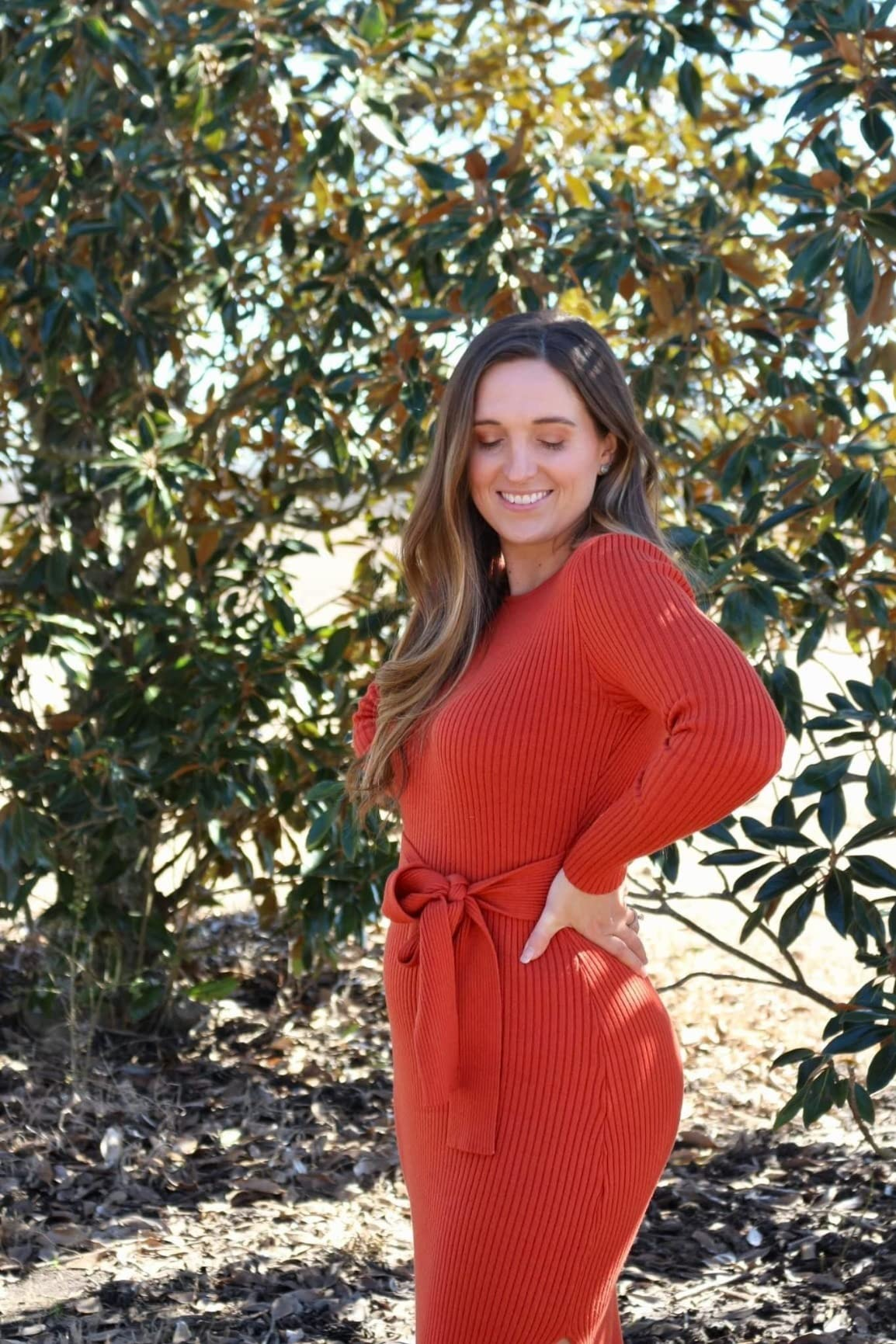 Person successful  a ribbed, cinched waist sweater formal  stands outdoors, smiling with closed eyes, surrounded by leafy trees