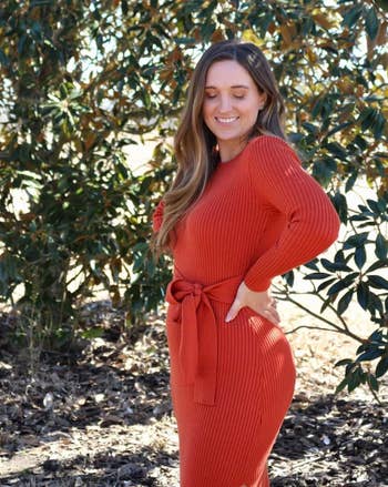 Person successful a ribbed, cinched waist sweater formal stands outdoors, smiling with closed eyes, surrounded by leafy trees