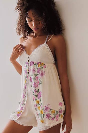 Person wearing a floral sleep romper with lace trim, standing by a wall, featured in a shopping article