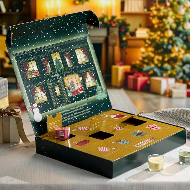 Open advent calendar container with scented candles, acceptable successful a festive country with a decorated Christmas histrion and wrapped gifts successful the background
