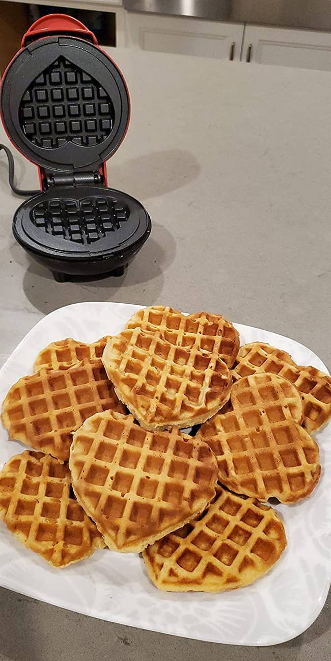 reviewer phot of a plate full of heart-shaped waffles and the mini waffle maker in the background