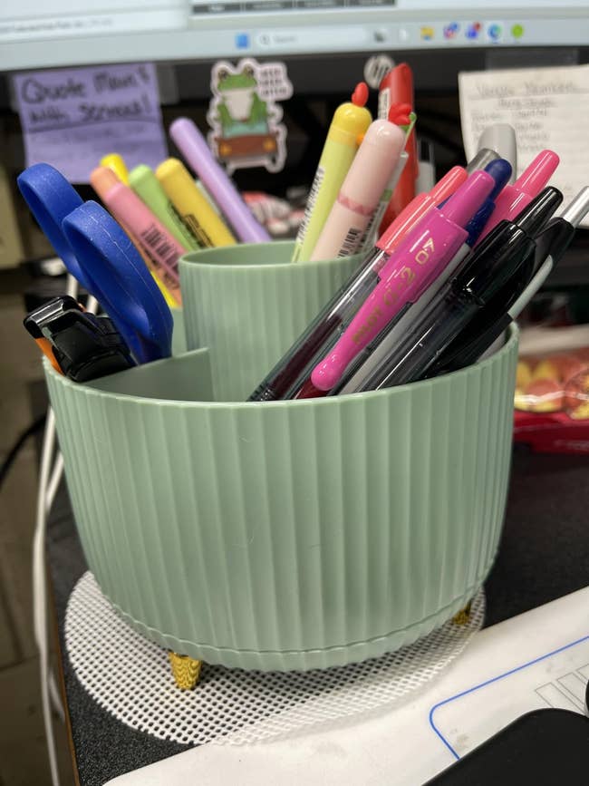 Organized table  setup with a greenish  pen holder containing assorted pens, pencils, and scissors, acceptable   connected  a tidy workspace
