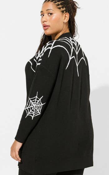 The same model showing the back of the cardigan with spider web designs on the back