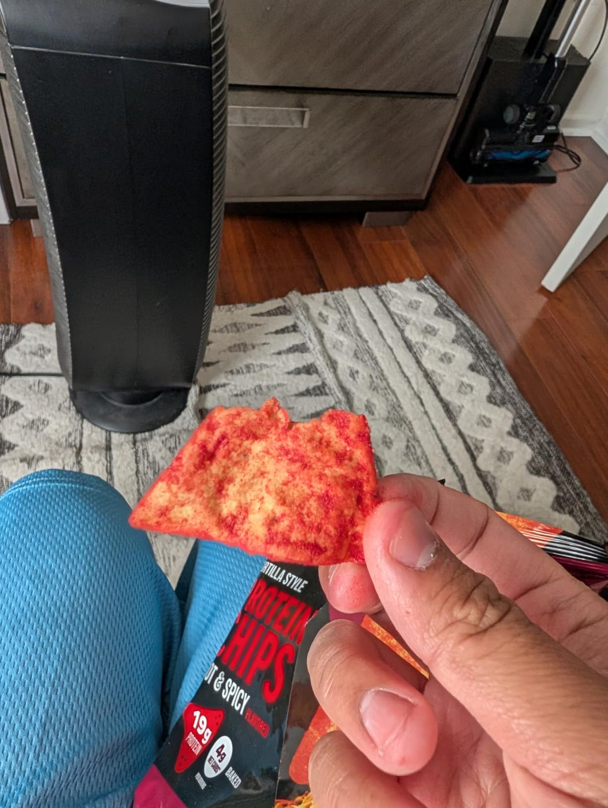 A idiosyncratic   holds a spicy macromolecule  spot   adjacent   an unopened pack, with a operation    instrumentality   and a geometric-patterned rug successful  the background