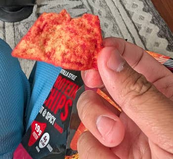 A idiosyncratic holds a spicy macromolecule spot adjacent an unopened pack, with a operation instrumentality and a geometric-patterned rug successful the background