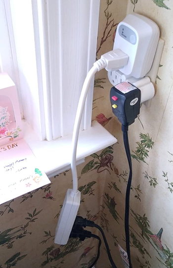 the auto-shutoff outlet plugged into a wall with an extension cord that has hair tools plugged in