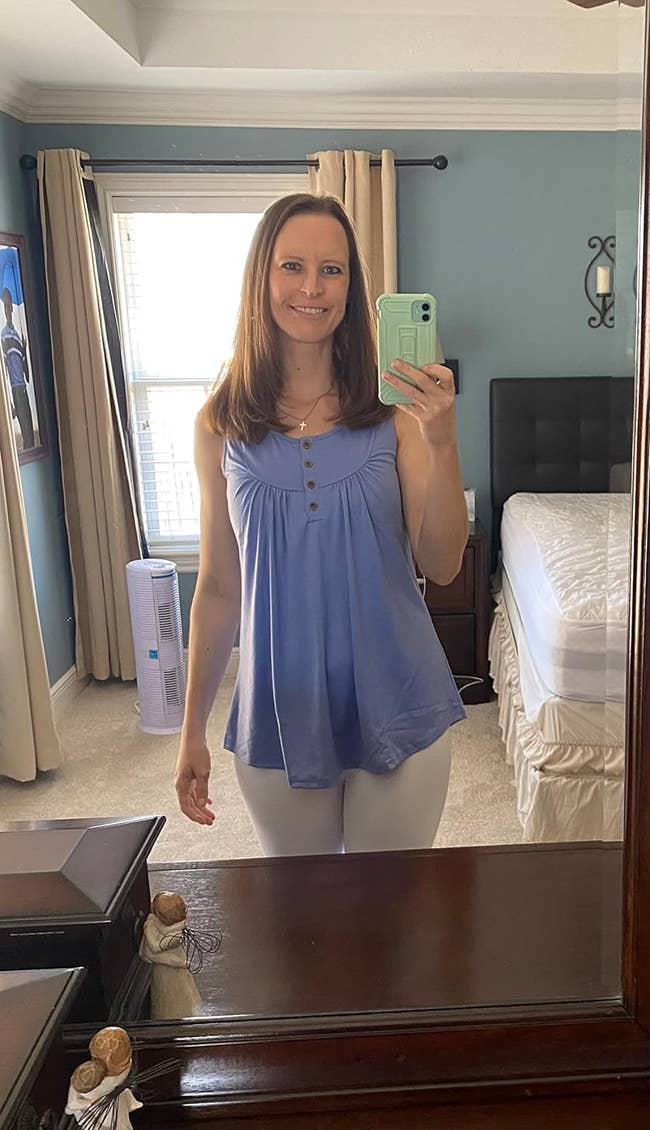 Woman in a casual blue top and white pants taking a mirror selfie, potentially for a fashion blog