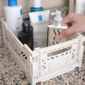 Hand organizing toiletries successful a achromatic handbasket connected a speckled countertop