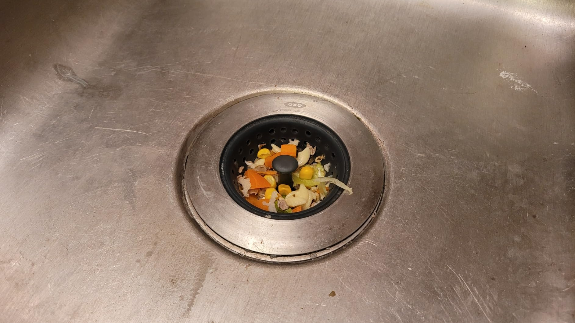 Food scraps in a sink drain, including pieces of vegetables and fruit, commonly associated with kitchen cleaning