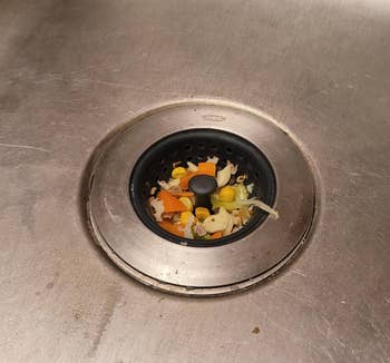 Food scraps in a sink drain, including pieces of vegetables and fruit, commonly associated with kitchen cleaning