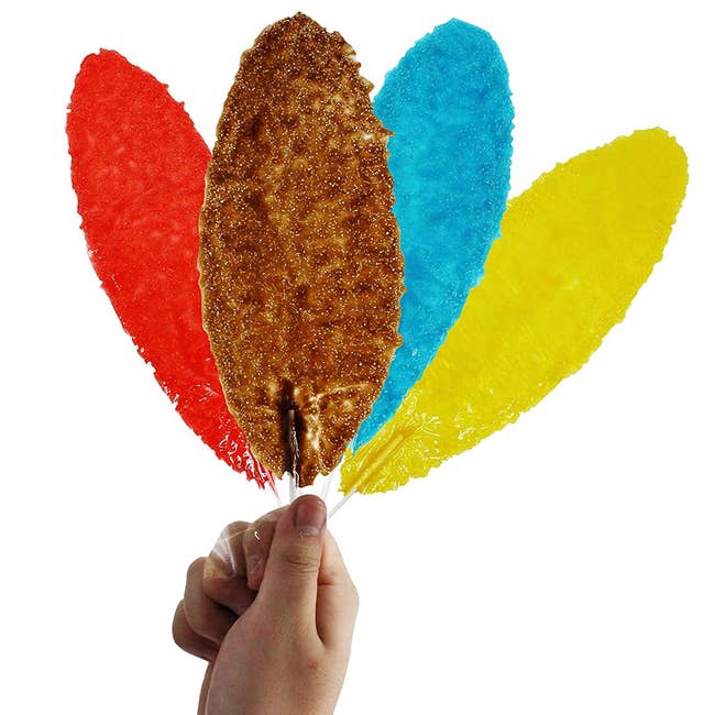a hand holding four slaps lollipops in red, brown, blue, and yellow