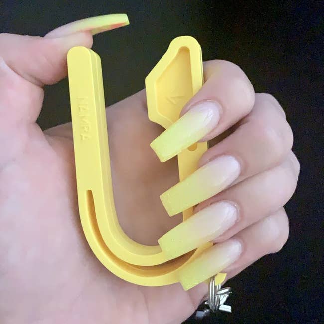 A manus  with long, manicured nails holds a yellowish  integrative  tool, perchance  for buying  container  handles oregon  akin  purposes