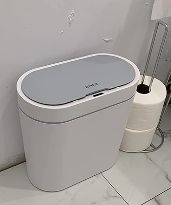 Small white oval shaped trashcan in a bathroom 