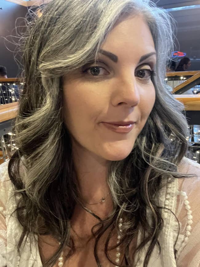 Person taking a selfie, wearing a achromatic  outfit with lace details and styled, wavy hair