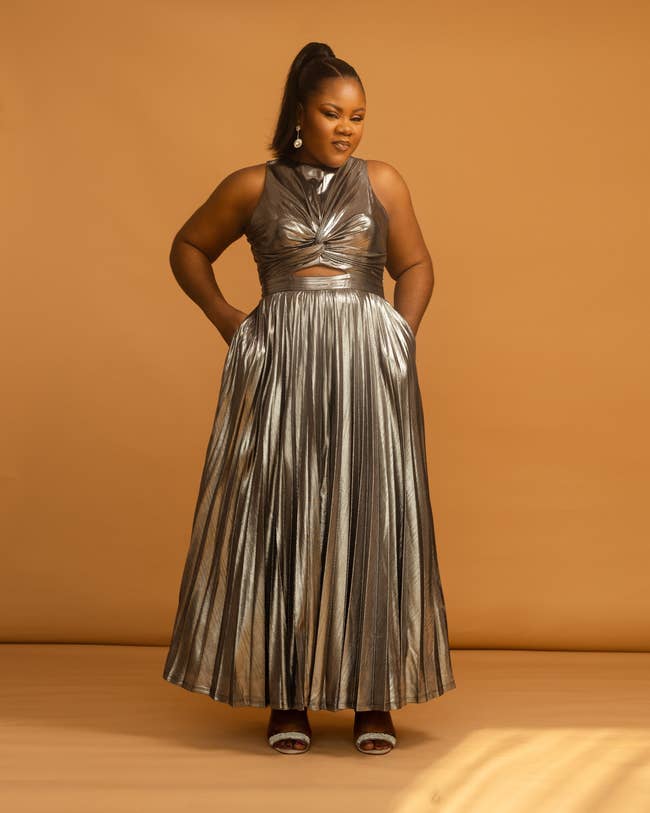 Woman in a metallic halter-neck dress with pleated skirt, posing confidently for a fashion-related article