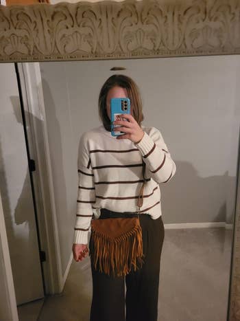 Person taking a mirror selfie wearing a striped sweater and wide-leg pants, holding a fringed crossbody bag