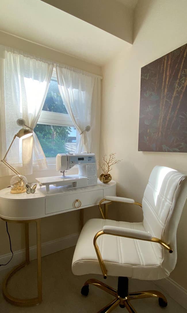A home office with a white desk and the chair in white with gold accents