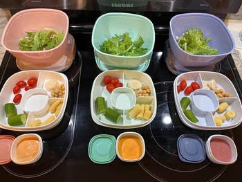 Three compartmentalized lunch trays contain assorted foods ready for meal prep