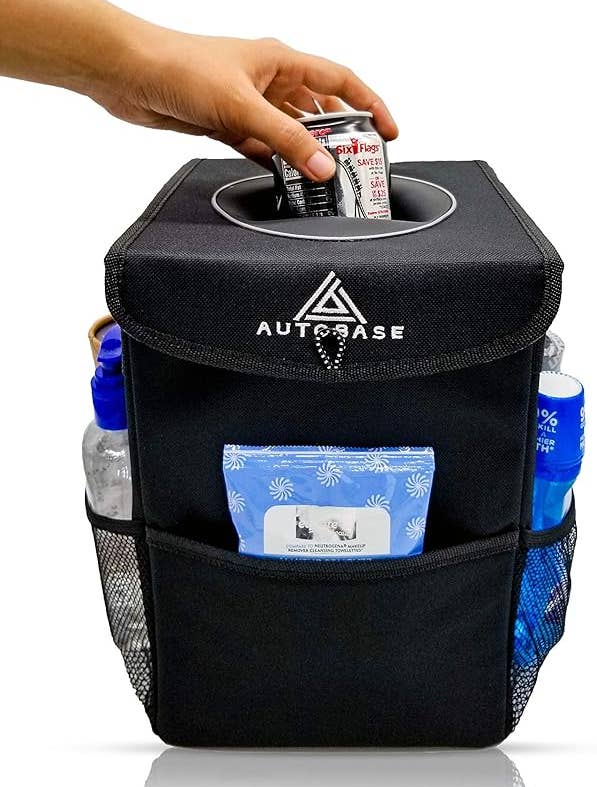 The car trash can shown with a model's hand placing a can inside of it. The side pockets are filled with items like hand sanitizer and wipes.