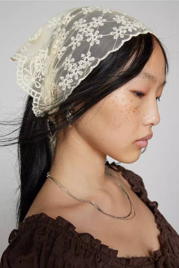 Model wearing a lace headscarf and brownish  off-shoulder top, showcasing delicate accessories