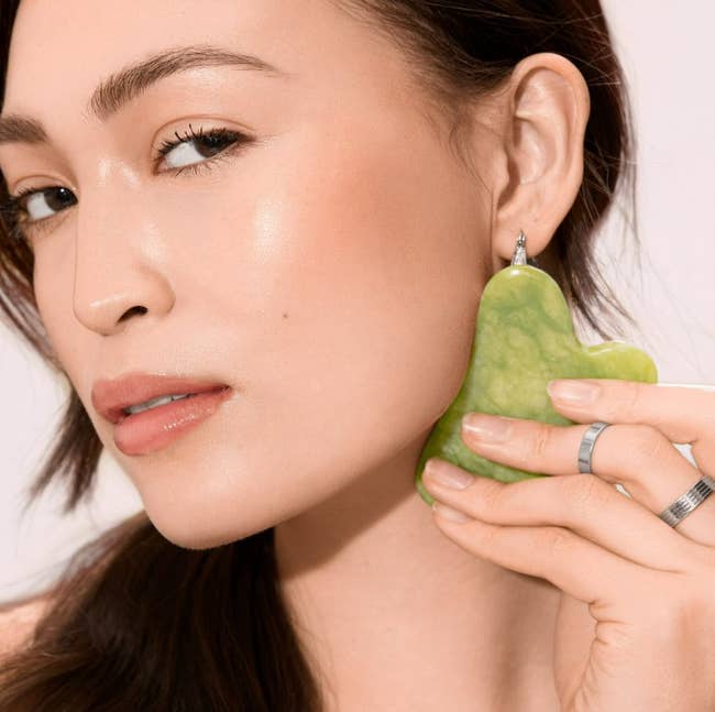 Person utilizing a jade gua sha instrumentality   connected  their face, demonstrating a skincare technique