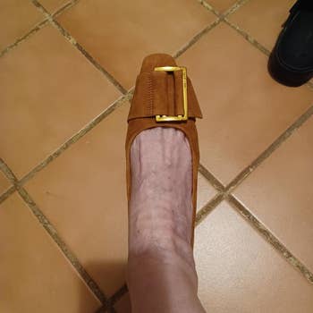A person's ft wearing a stylish suede level footwear with a ample buckle design, lasting connected a tiled floor