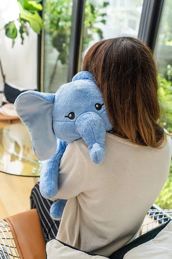 Model hugging a medium sized blue elephant plush 