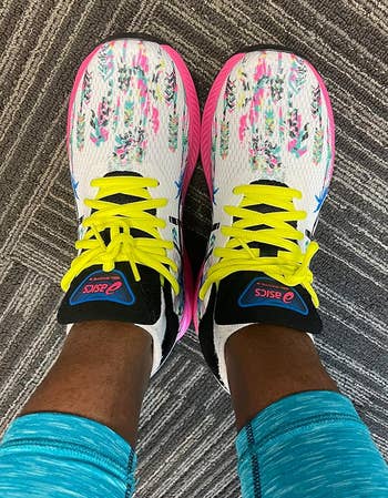 Person wearing ASICS sneakers with vibrant patterns and bright yellow laces, viewed from above