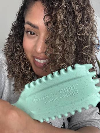 reviewer smiling, holding a wavy-edged detangling hairbrush labeled 
