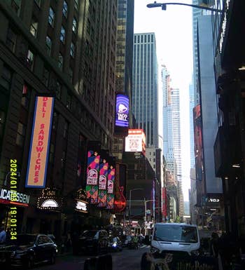 City thoroughfare  country   with gangly  buildings and agleam  neon signs for Taco Bell and Dell Sandwiches, bustling with pedestrians and vehicles