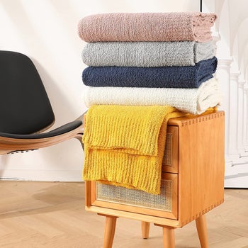 a stack of throw blankets in assorted colors on top of an end table
