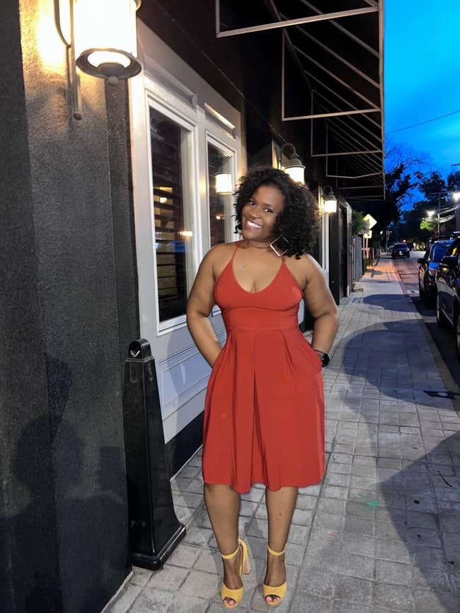 Person successful  a sleeveless formal  and heels poses connected  a sidewalk adjacent   a storefront, smiling astatine  the camera. Stone pavements enactment     the walkway
