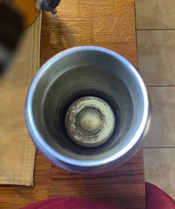 Moldy interior of a stainless steel tumbler on a wooden countertop, highlighting the importance of regular cleaning for reusable drinkware