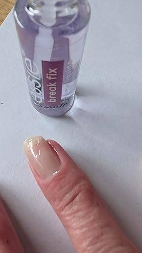 A close-up of a hand with nail polish being applied. A bottle labeled