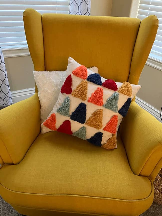 reviewer image of the colorful tufted pillow on a yellow armchair