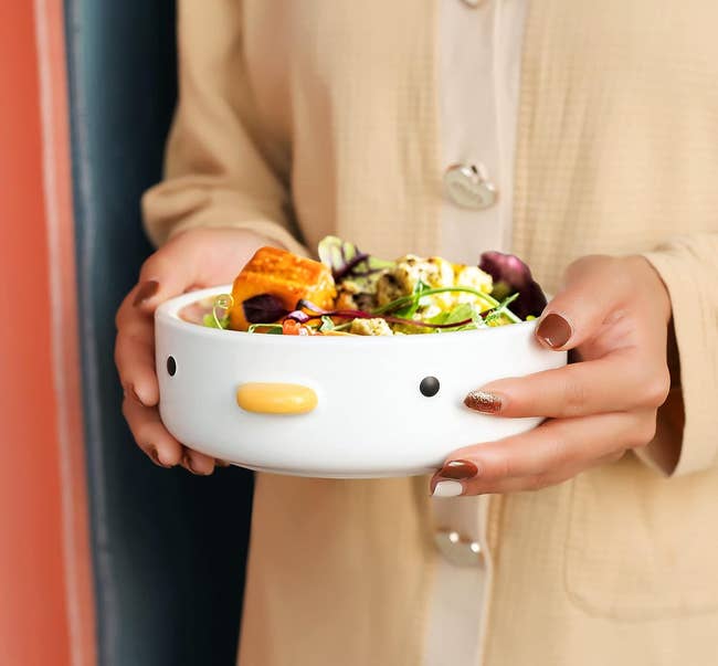 A round flat bowl with a duck face on it full of salad 