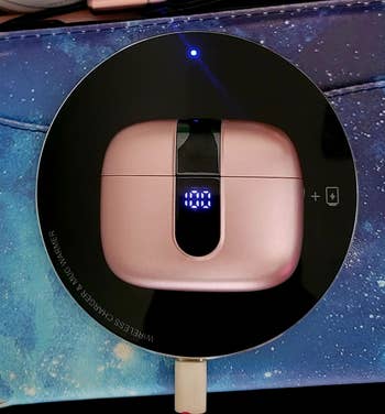 Wireless earbud case with a digital display, charging on a round black wireless pad, featured in a shopping article