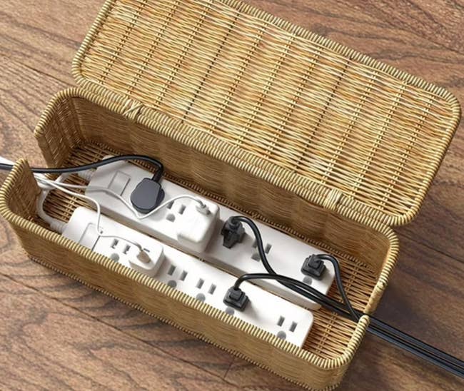 Woven handbasket holding powerfulness strips and assorted cables, organized and concealed connected a woody surface