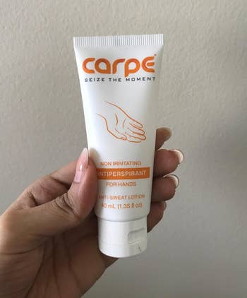 reviewer holding the white and orange tube of antiperspirant lotion