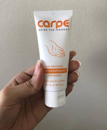reviewer holding the white and orange tube of antiperspirant lotion