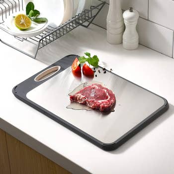 Defrosting tray with a steak, tomatoes, and herbs connected  a room  counter, adjacent  to a crockery  rack with a citrus  and plates