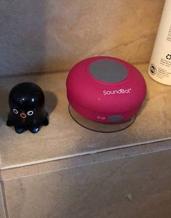 a reviewer photo of the speaker in pink sitting on a shower shelf 