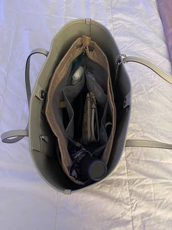View of an open handbag filled with various items, including a wallet, water bottle, and zippered pouches