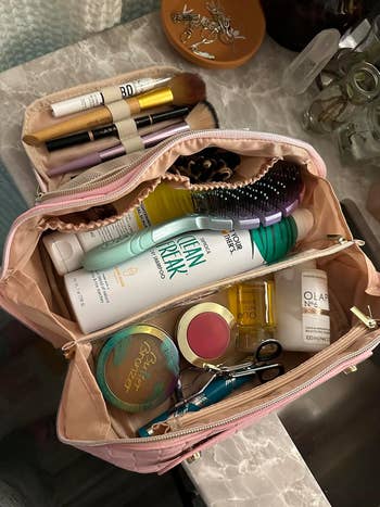 Buka tas riasan dengan kuas, maskara, sampo kering, semprotan wajah, perona pipi, dan benda kecantikan lainnya di permukaan marmer